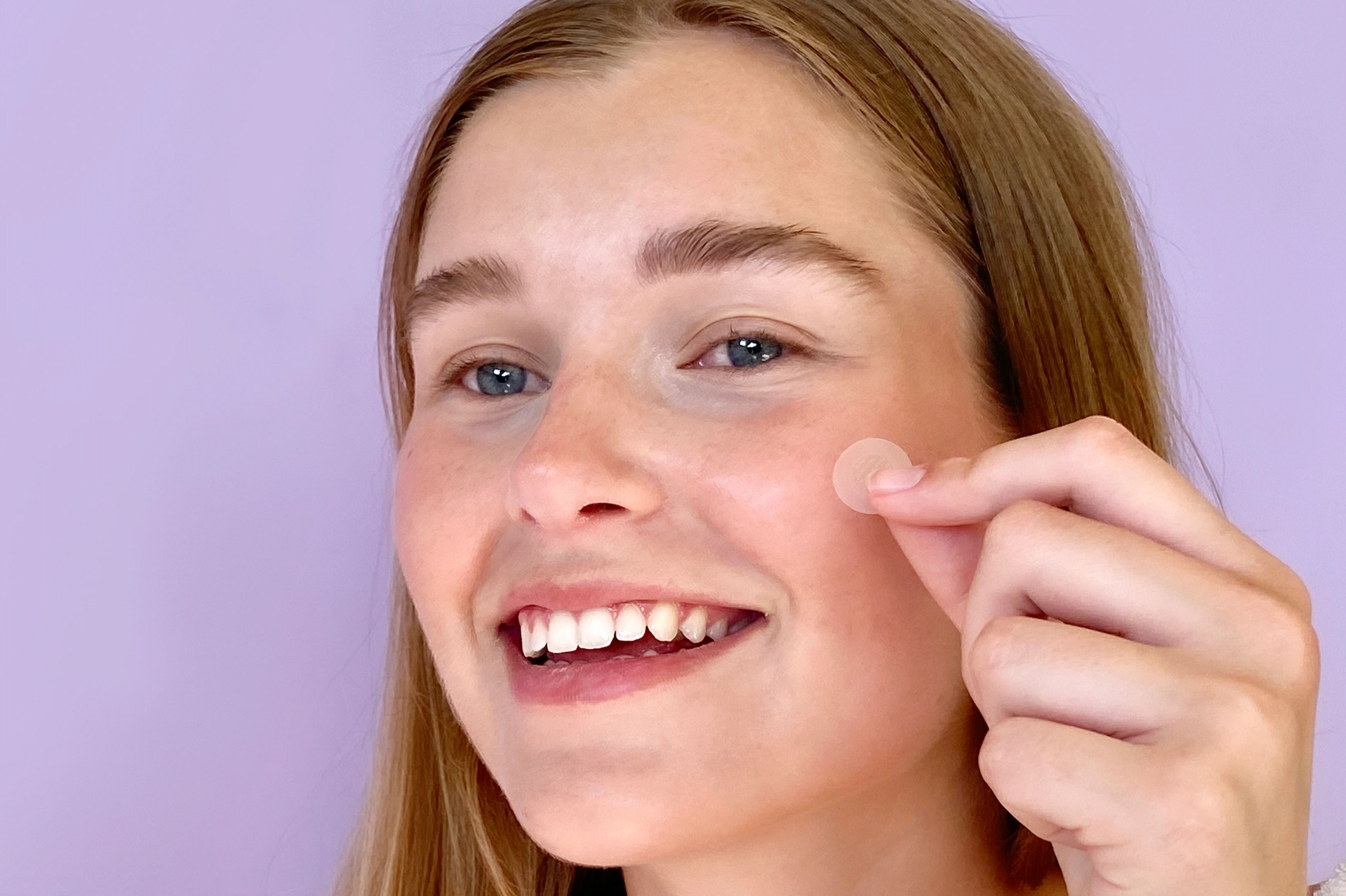 Girl smiling holding up pimple patch to her face